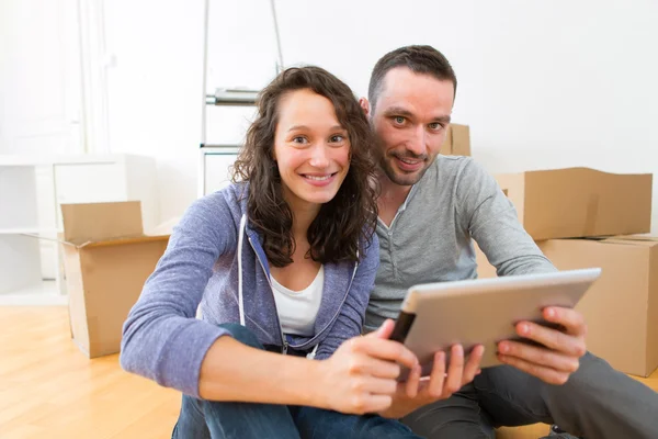 Vista de una pareja joven usando tableta mientras se mueve en un piso nuevo —  Fotos de Stock