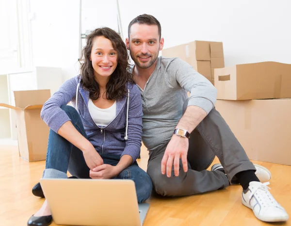 Young couple using laptop while moving in new flat — Stock Photo, Image