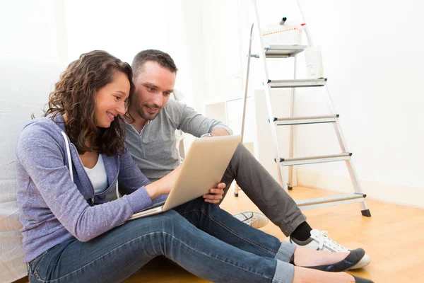 Young couple using laptop while moving in new flat — Stock Photo, Image