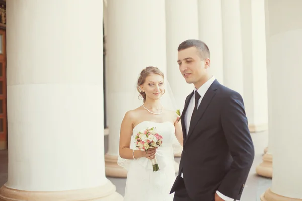 Novia y novio posando cerca de las columnas blancas — Foto de Stock