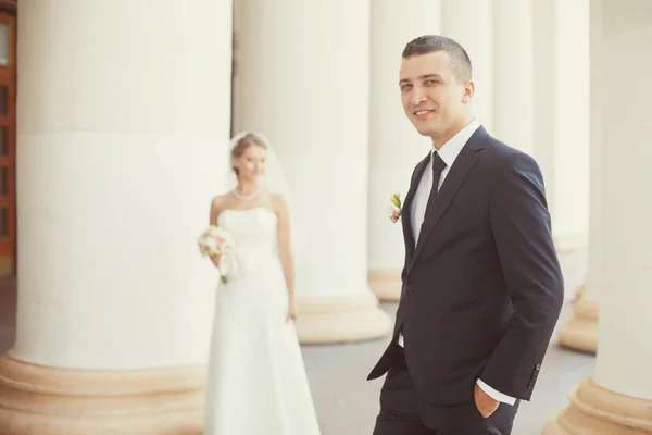 Novia y novio posando cerca de las columnas blancas — Foto de Stock