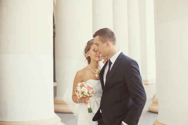 Novia y novio posando cerca de las columnas blancas — Foto de Stock