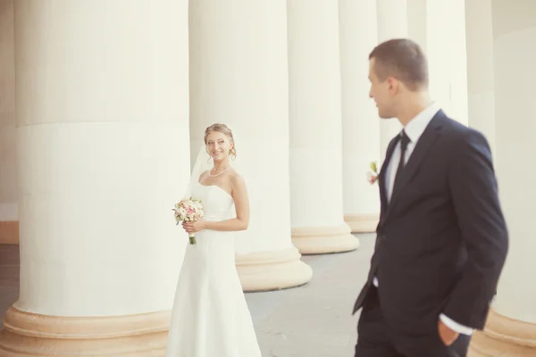 Novia y novio posando cerca de las columnas blancas — Foto de Stock