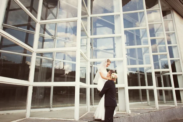 Жених и невеста позируют возле стеклянного здания — стоковое фото