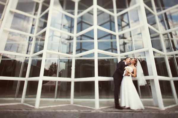 Bride and groom posing near the glass building