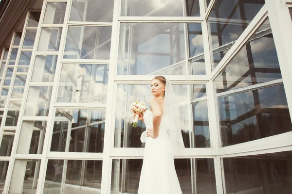 Невеста с букетом возле стеклянного здания — стоковое фото