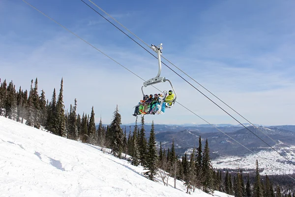 Seis snowboarders montan en el ascensor sobre un fondo de montañas —  Fotos de Stock