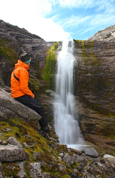 Girl sitting on a rock and looking at the beautiful waterfall — Stock Photo, Image