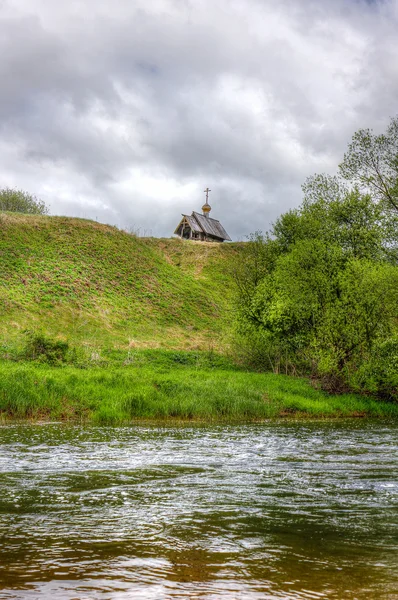 Fiume e una chiesa di legno sulla collina — Foto Stock