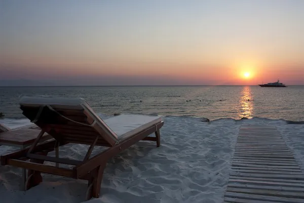 Espreguiçadeira vazia ao pôr do sol na praia com barco — Fotografia de Stock