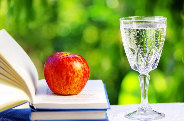 Apfel auf offenem Buch und Wasserbecher — Stockfoto