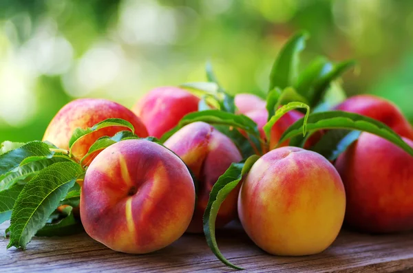 Ripe peaches and leaves on table — Stock Photo, Image