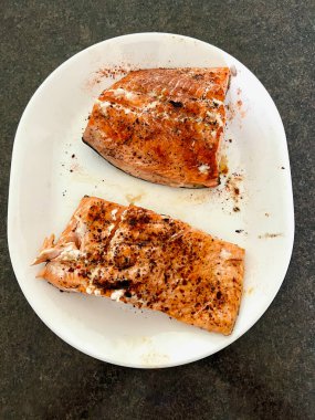 Baharatlı somon balığı tabakta, arka planda karanlık bir masa.