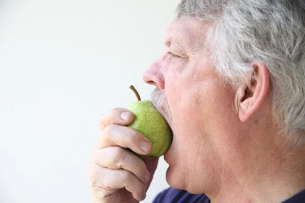 Older man bites into pear — Stock Photo, Image