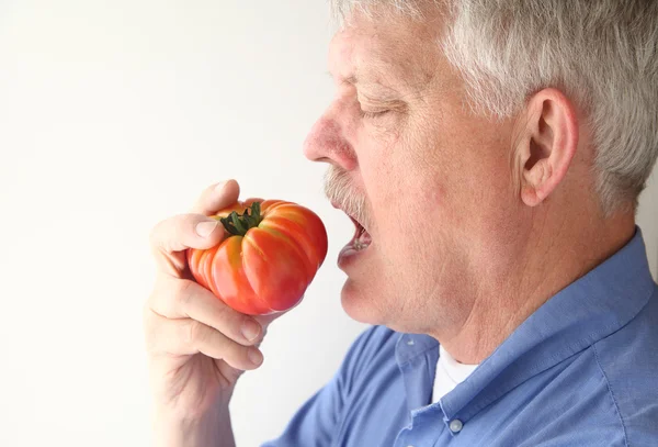Homem idoso comendo tomate grande — Fotografia de Stock