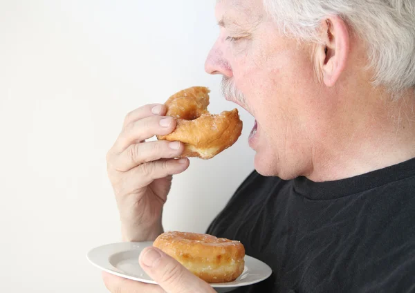 Літній чоловік їсть глазурований пончик — стокове фото
