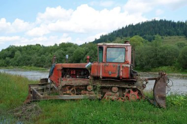 Kırmızı traktör nehrin yanında duruyor.