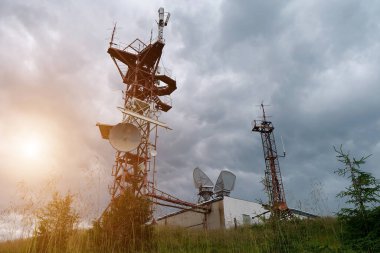 Dağlardaki meteoroloji istasyonlarının antenleri, fırtına bulutları ve batan güneş
