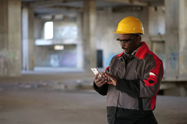 Afrikansk Amerikansk Arbetare Gul Hatt Står Byggarbetsplatsen Håller Händer Smartphone — Stockfoto