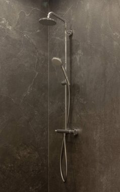 Part of the bathroom with a view of the hand shower and tiles on the wall.