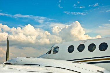 Açık mavi gökyüzüne ve kabarık beyaz bulutlara karşı uçağın ön görüntüsü.