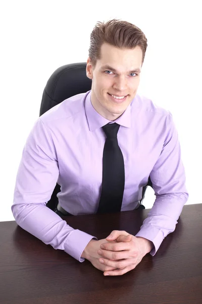 Cheerful young businessman sitting at his desk and smiling into — Stock Photo, Image