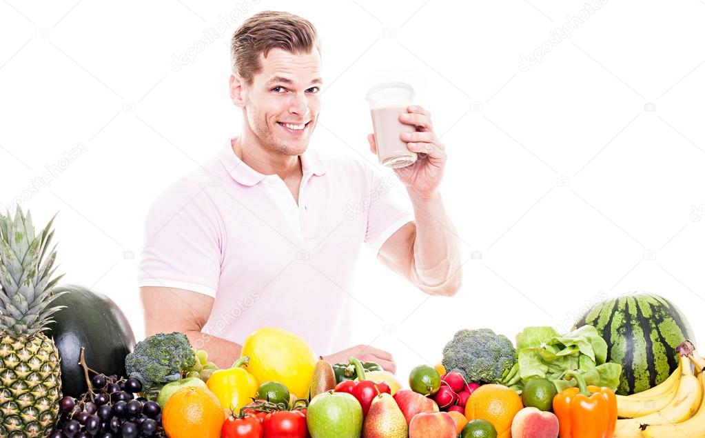 Athletic man drinking a protein shake behind a table full of veg