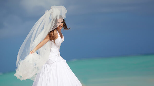 The bride with a veil on the beach in the sky and blue sea.