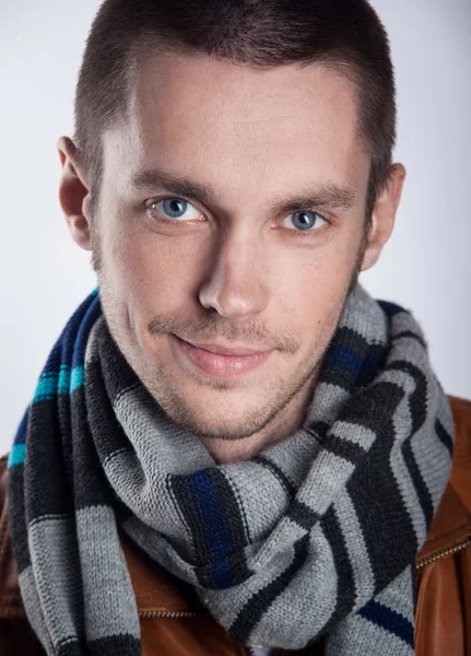 Portret van een jonge man in bruine jas met gestreepte sjaal over grijze achtergrond. Close-up. studio opname — Stockfoto