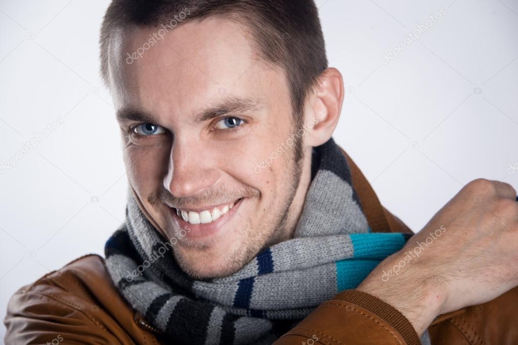 Portrait of young man in brown jacket with striped scarf over gray background. Close-up. studio shot