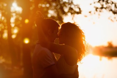young beautiful couple embracing on a white background of a sunset clipart