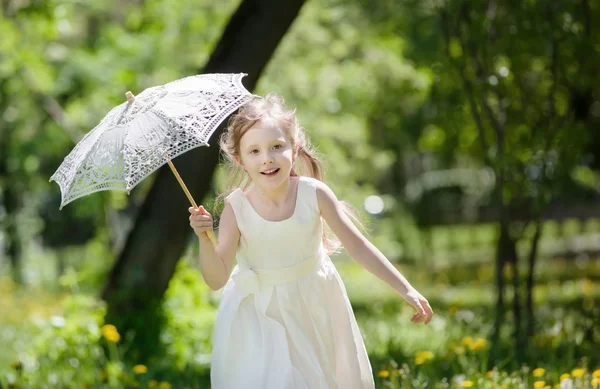 Девушка с летним кружевным зонтиком играет в парке — стоковое фото