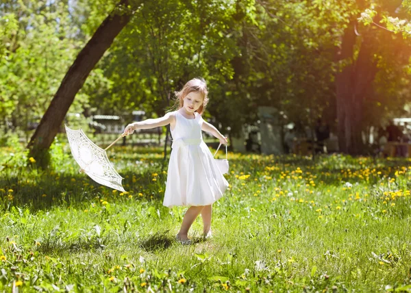 Flicka med en sommar spetsar paraply spelar i parken — Stockfoto