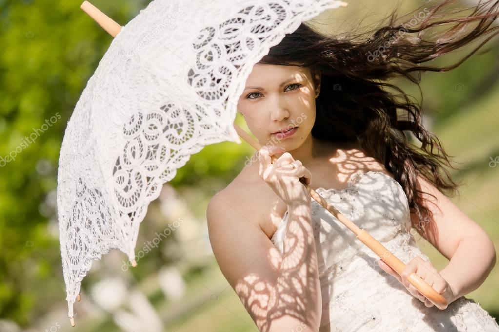 portrait of the bride with decorative umbrella against background green summer park
