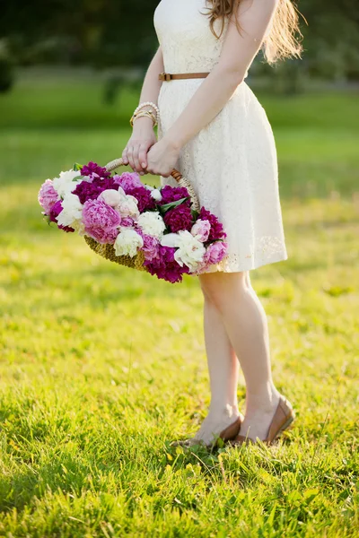 Ragazza in abito bianco con in mano un cesto con peonie — Foto Stock