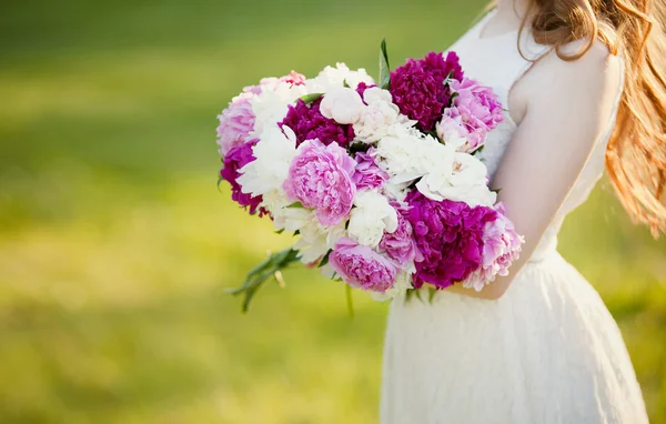 Meisje in een witte jurk met een mand met pioenrozen — Stockfoto