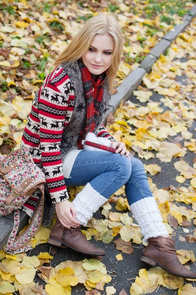 Jeune femme blonde assise sur des feuilles jaunes dans le parc — Photo