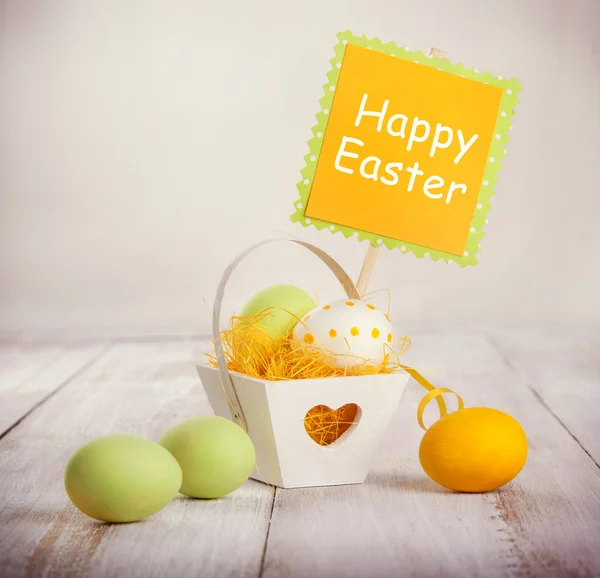 Huevos coloridos de Pascua en una cesta decorativa sobre fondo de madera — Foto de Stock