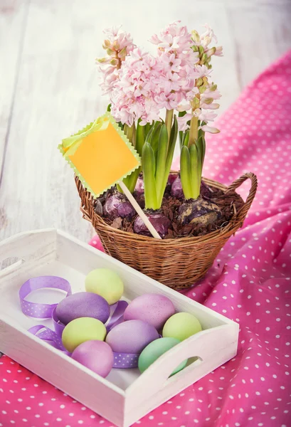 Tray with Easter eggs and a basket of hyacinths on a wooden table — Stock Photo, Image