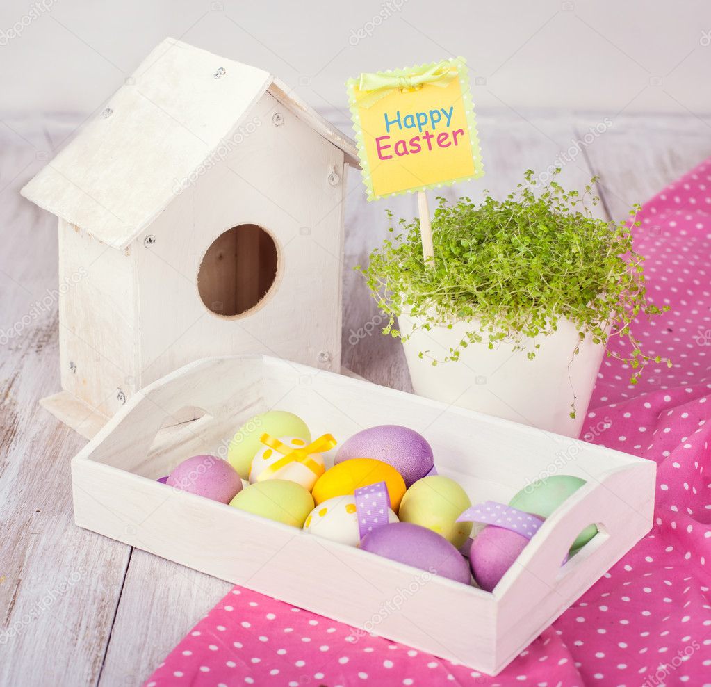 Easter eggs, green grass, wooden birdhouse on a white table