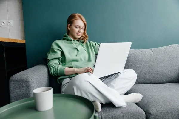 Молода руда біла жінка в зеленому светрі в домашніх покупках онлайн за допомогою ноутбука — стокове фото