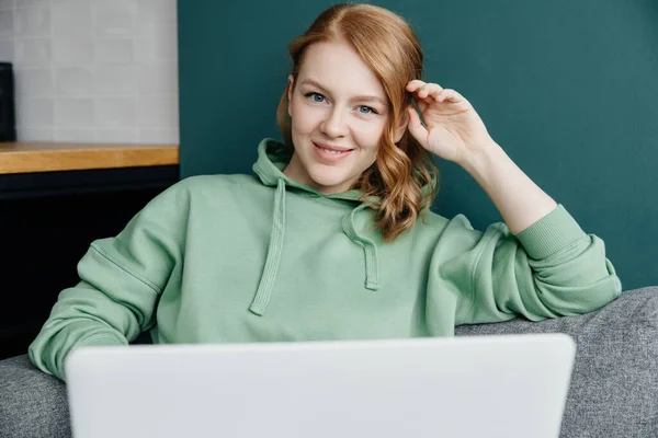 Портрет молодої красивої білої жінки, одягненої в зелений светр, що працює вдома за допомогою ноутбука — стокове фото
