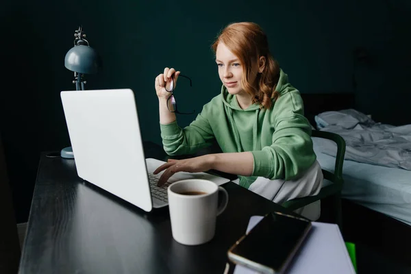 Genç kızıl saçlı kadın evde dizüstü bilgisayar kullanarak çalışıyor. — Stok fotoğraf