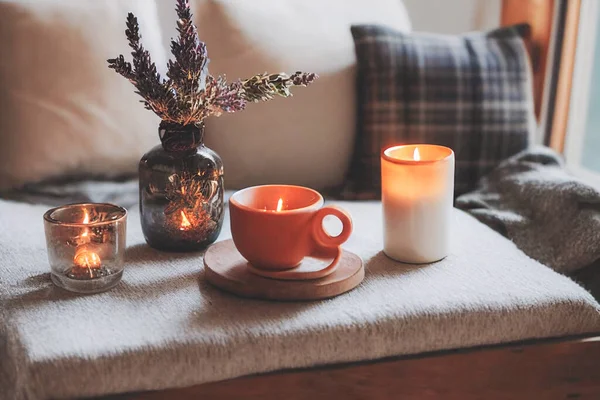 3D render of Autumn hygge home decor arrangement, concept of hygge and coziness, burning white fragrance candle on tray and lavender branches in a bottle vase on table at cozy home