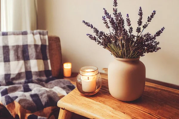 3D render of Autumn hygge home decor arrangement, concept of hygge and coziness, burning white fragrance candle on tray and lavender branches in a bottle vase on table at cozy home