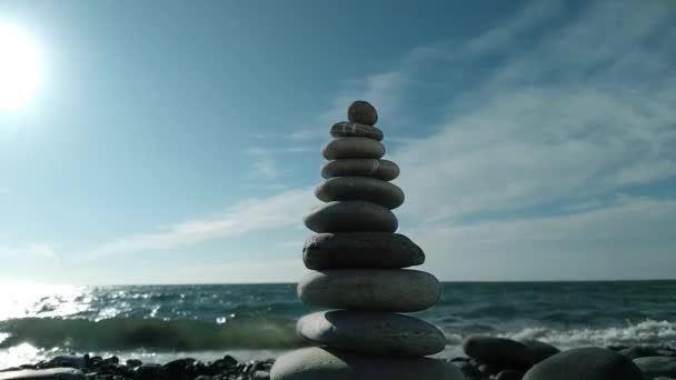 해변에서는 균형잡힌 조약돌 모양의 피라미드가 바람에 흔들리면서 파도의 배경을 이루고 — 비디오