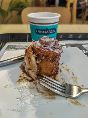 Saint-Petersburg, Rusya - 21 Haziran 2021. Tek kullanımlık bir fincan çay ve tarçınlı kek Cinnabon Kafe 'deki masada çatal ve bıçakla başladı ve bitti.