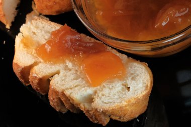 Şeftali reçelli bir dilim beyaz çörek siyah bir arka planda yatıyor.