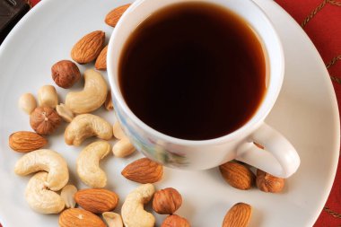 Bir fincan koyu siyah çay, masada fındık ve kırmızı masa örtüsü.