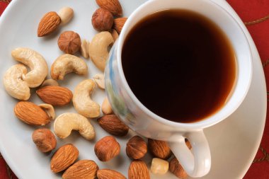 Bir fincan koyu siyah çay, masada fındık ve kırmızı masa örtüsü.